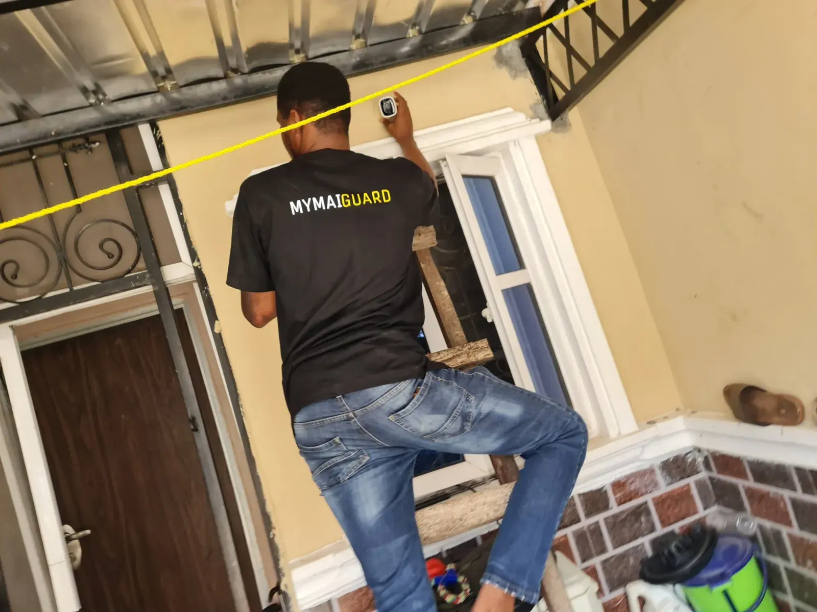 A MYMAiGUARD engineer in a branded T-shirt fixing a security camera above a doorway