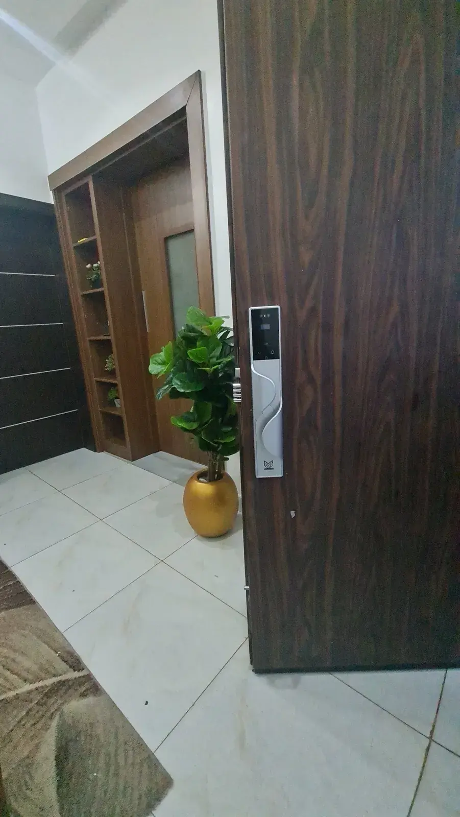 A silver MYMAiGUARD face-recognition smart lock fitted on a dark wooden door, opening into a hallway