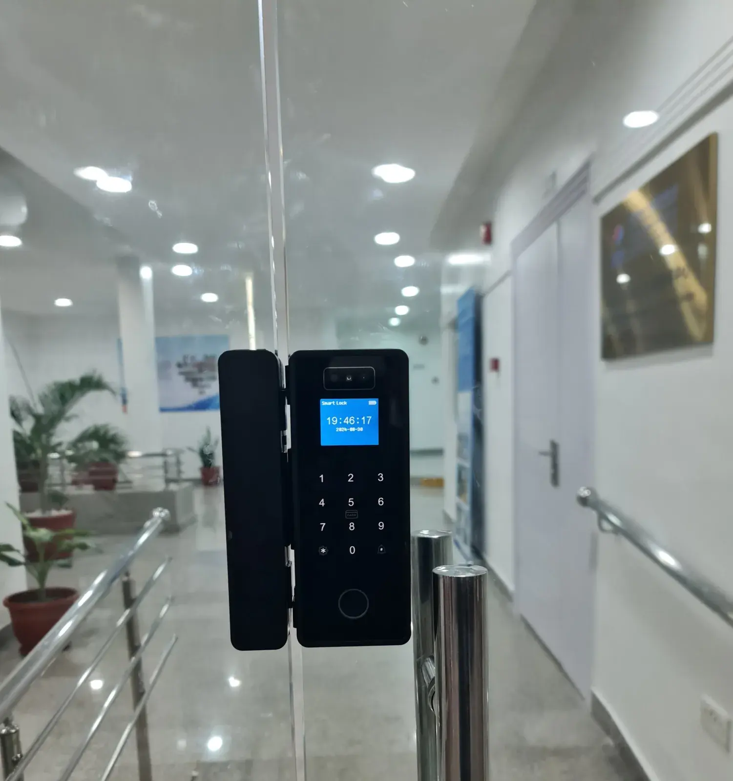 A MYMAiGUARD smart lock with keypad, fingerprint reader and screen clamped onto a frameless glass office door