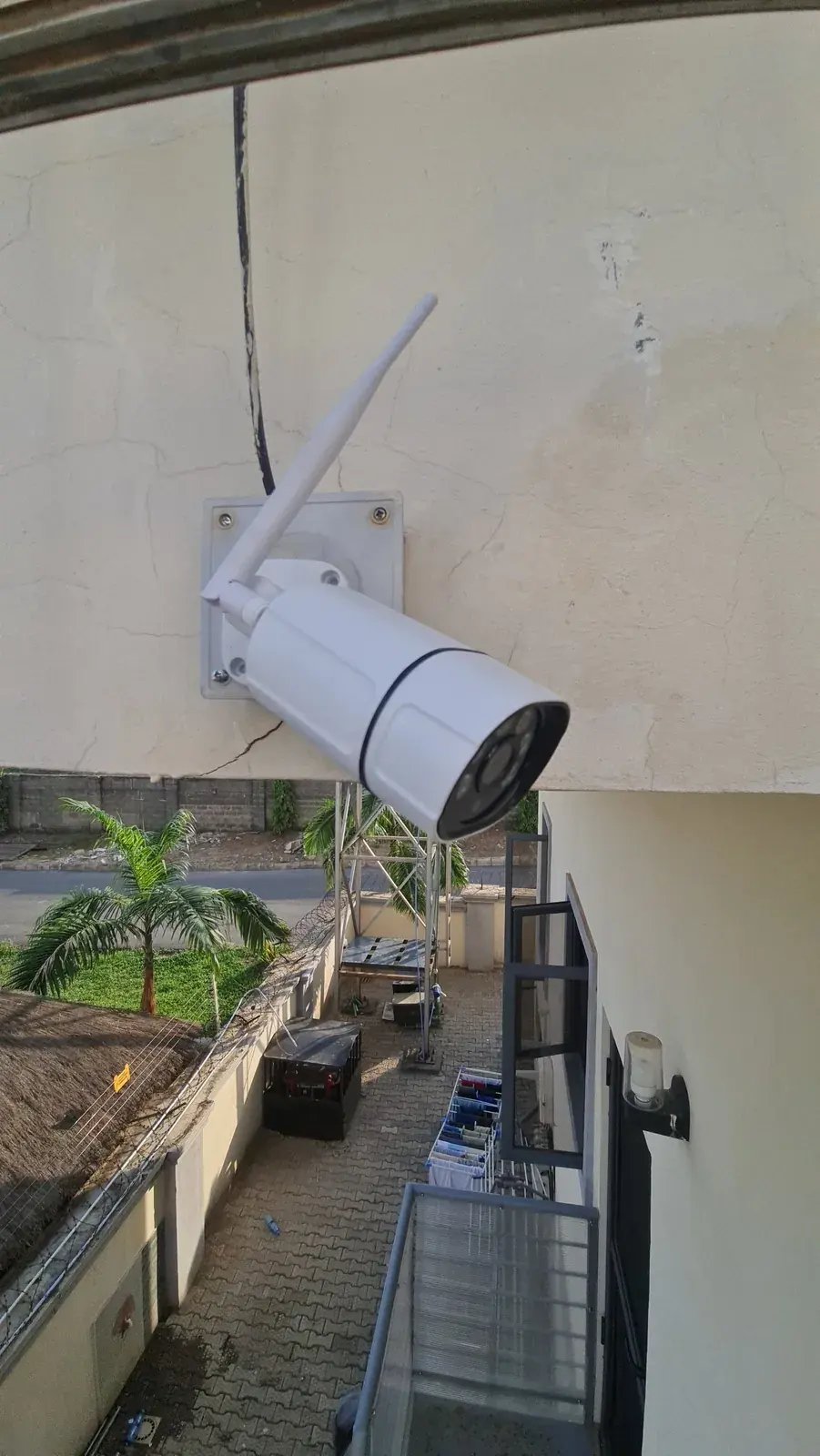 A MYMAiGUARD outdoor camera on an upper wall, looking down over a compound and gate