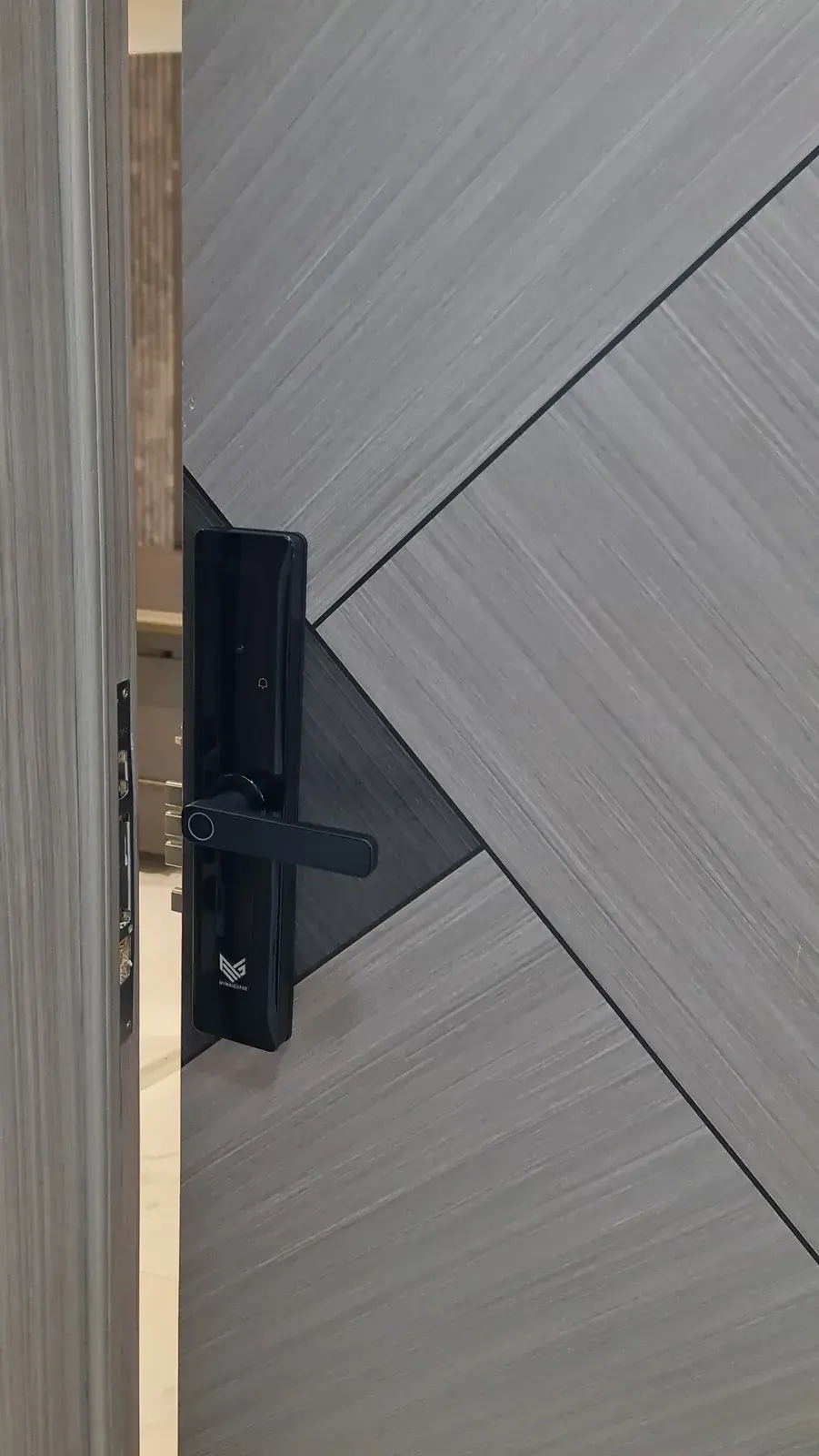 A black MYMAiGUARD-branded smart lock with a fingerprint reader in the handle, fitted on a grey apartment door