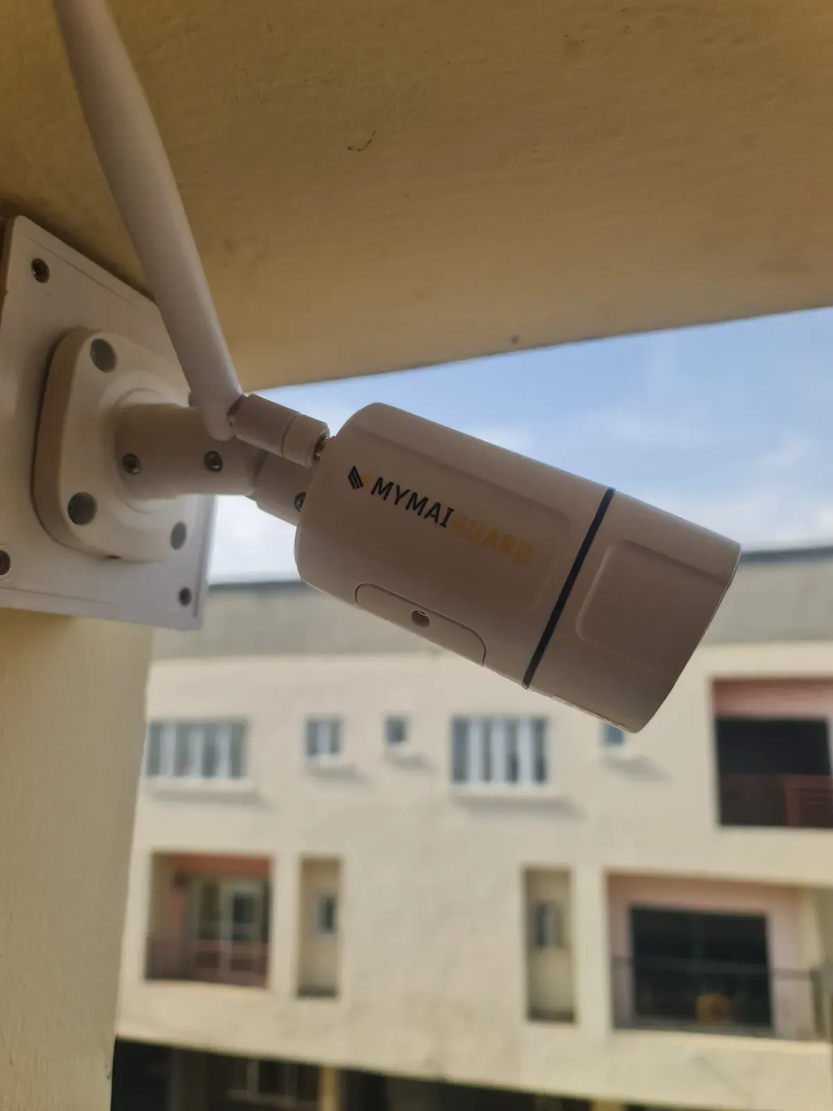 A white MYMAiGUARD WiFi bullet camera with antenna mounted under a roof overhang